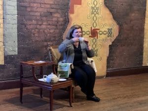 Breeda Miller as Mrs. Kelly drinking tea.